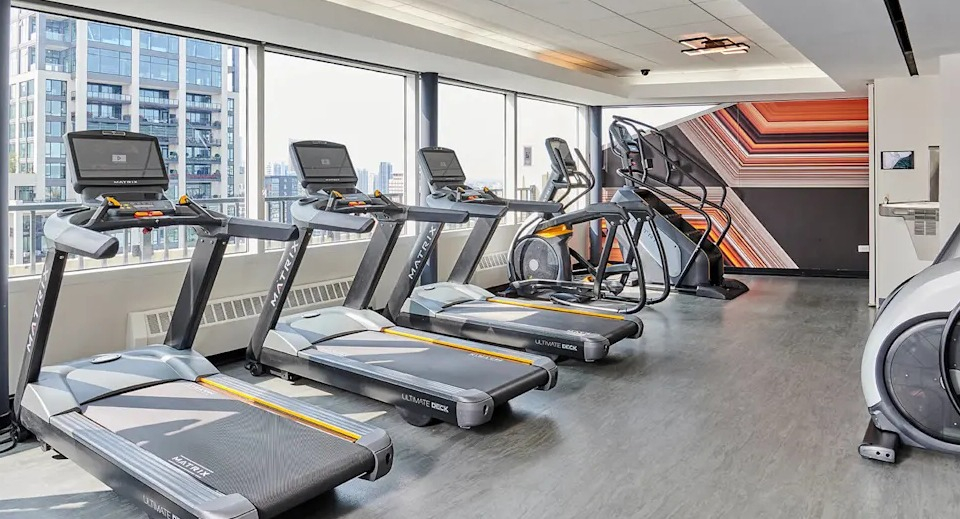 Modern fitness center equipped with multiple treadmills and cardio machines, offering city views through large windows at Two East Oak in Chicago