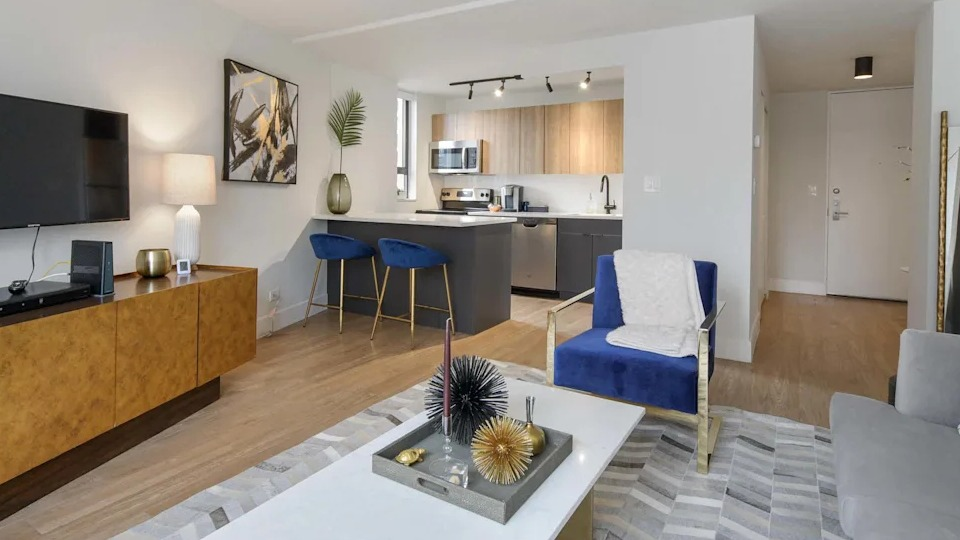 Open-concept living room flowing into a modern kitchen with an island, dark cabinetry, and sleek appliances at Two East Oak in Chicago