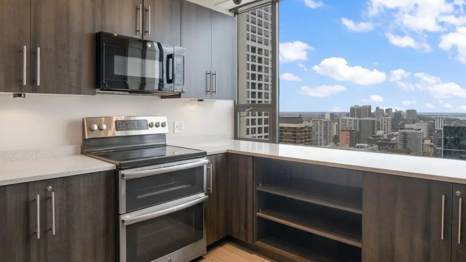 Modern communal kitchen with a large island, bar seating, dark wood cabinets, and sleek pendant lighting at Two East Oak in Chicago