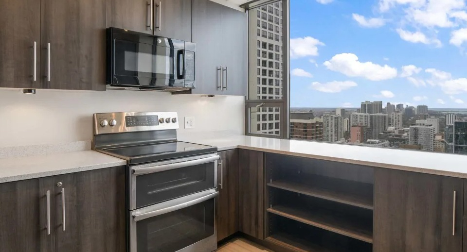 Modern communal kitchen with a large island, bar seating, dark wood cabinets, and sleek pendant lighting at Two East Oak in Chicago
