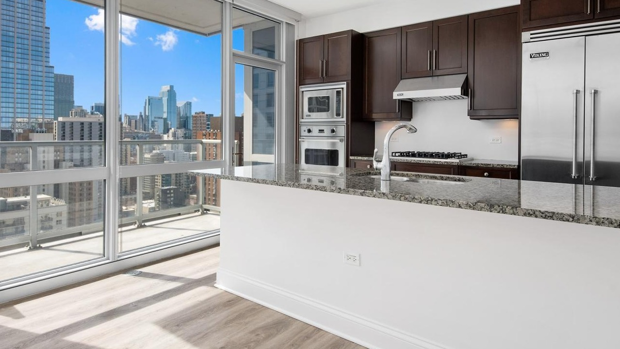 Modern kitchen with dark wood cabinets, granite countertops, and stainless steel appliances, offering a balcony with city views at Two West apartments in Chicago