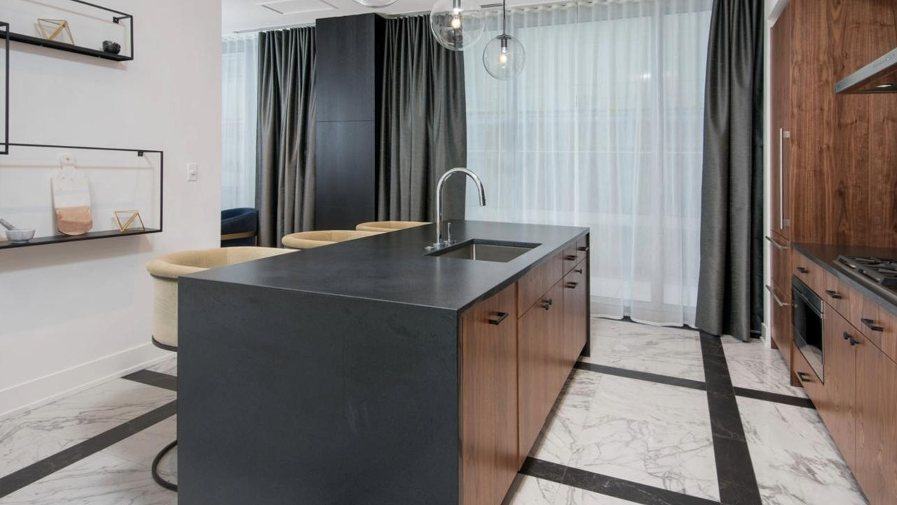 Sophisticated kitchen featuring rich wood cabinetry, a dark countertop island with bar stools, and modern pendant lighting at Two West apartments in Chicago