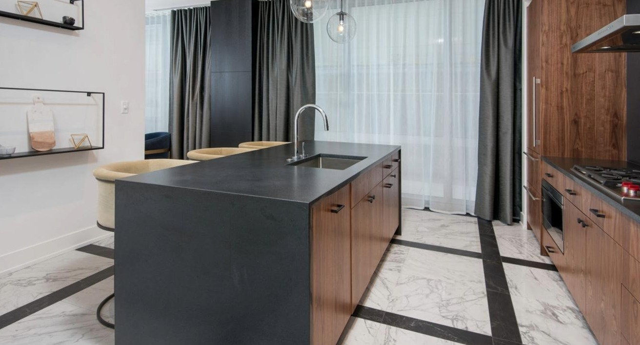 Sophisticated kitchen featuring rich wood cabinetry, a dark countertop island with bar stools, and modern pendant lighting at Two West apartments in Chicago