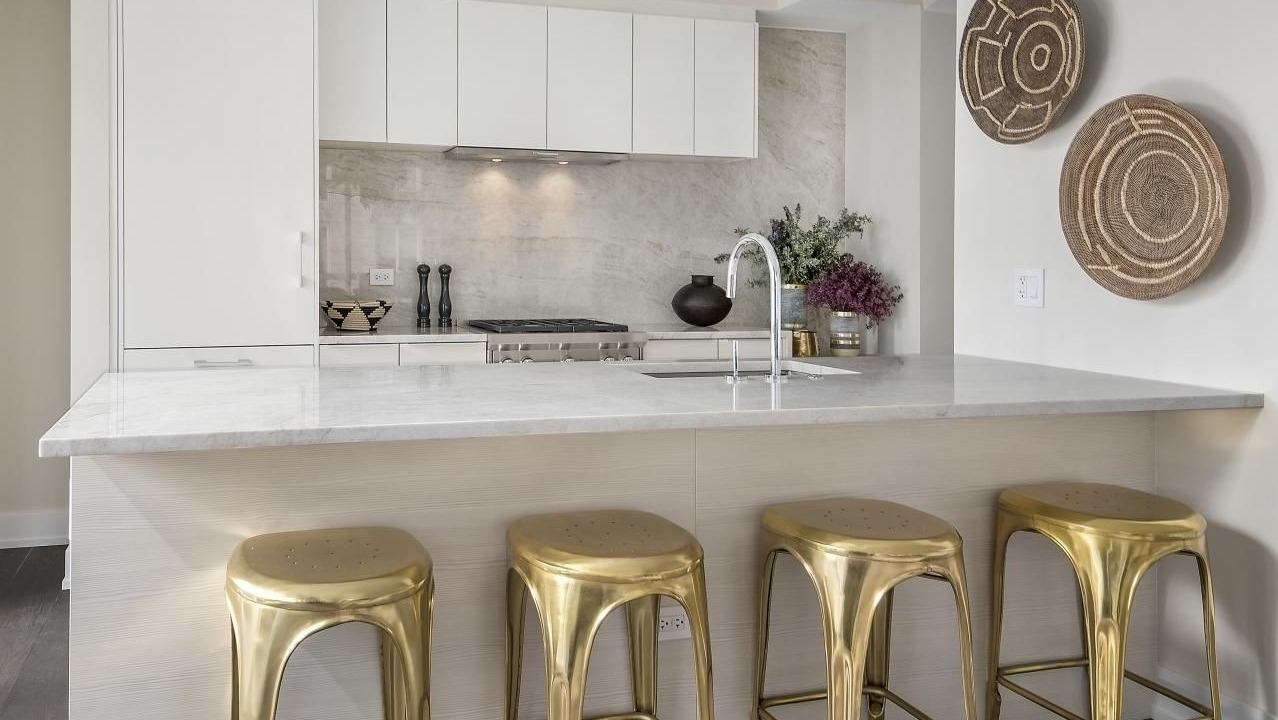 Contemporary kitchen with white cabinetry, marble countertops, and striking gold bar stools at Two West apartments in Chicago