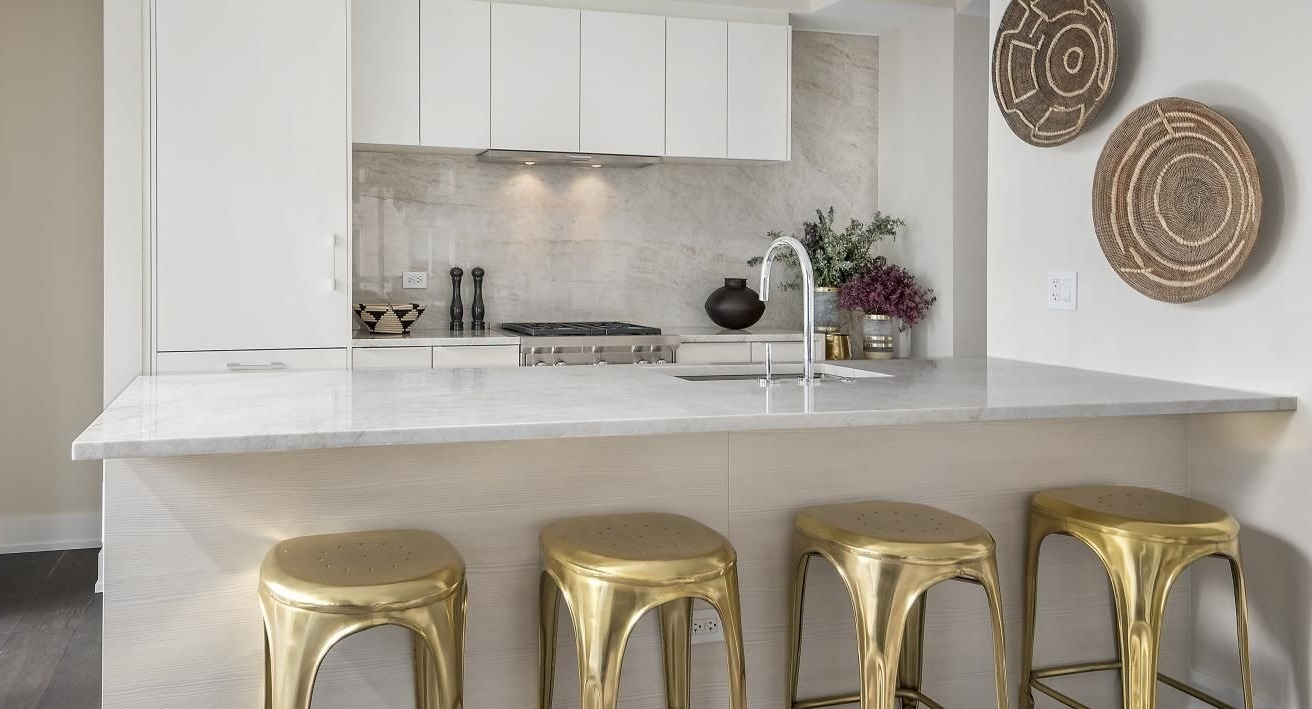 Contemporary kitchen with white cabinetry, marble countertops, and striking gold bar stools at Two West apartments in Chicago