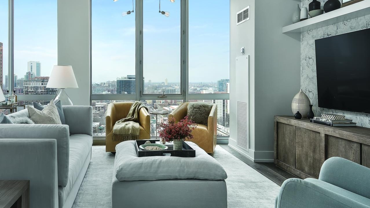 Cozy living room with light grey furniture, warm yellow armchairs, and expansive city views from Two West apartments in Chicago