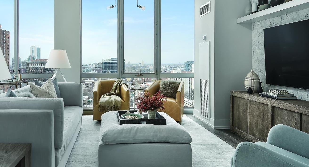 Cozy living room with light grey furniture, warm yellow armchairs, and expansive city views from Two West apartments in Chicago