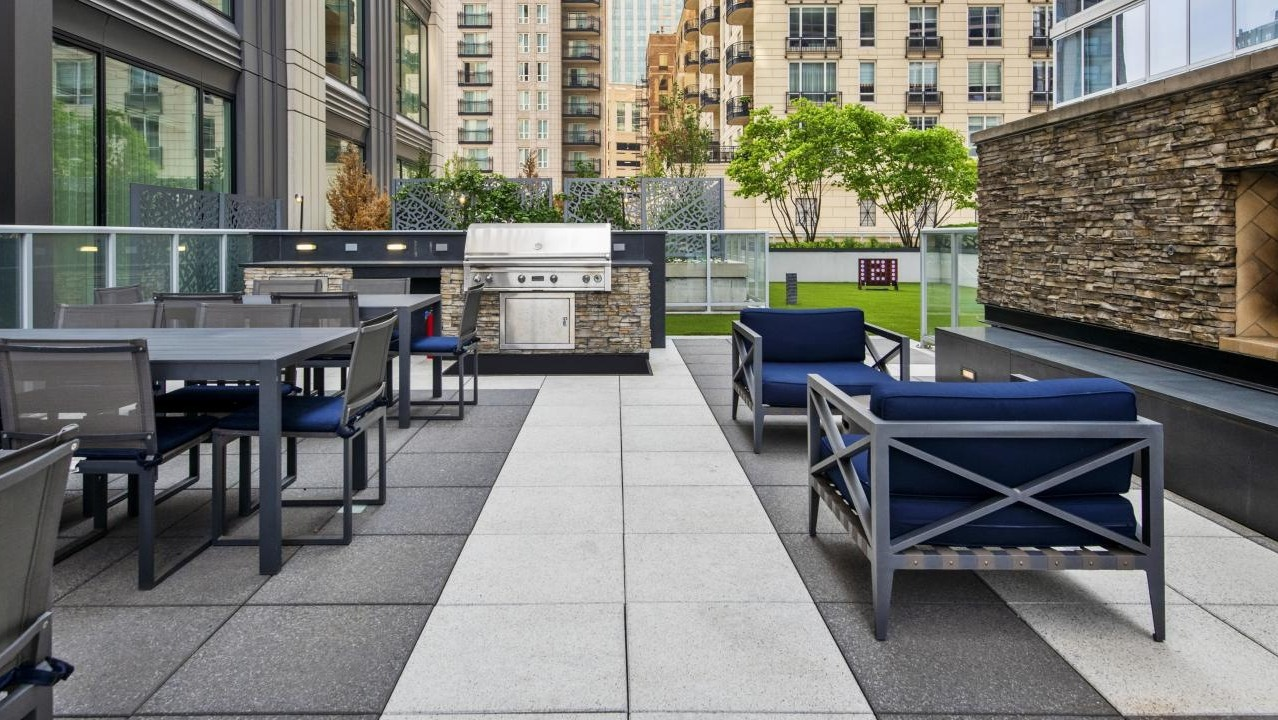 Upscale outdoor patio with comfortable seating, a stone fireplace, and a built-in grill area at Two West apartments in Chicago