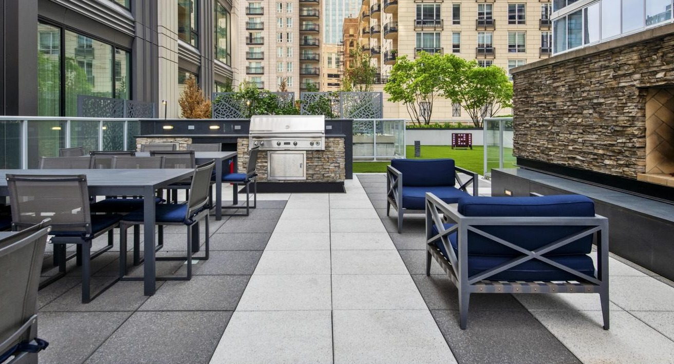 Upscale outdoor patio with comfortable seating, a stone fireplace, and a built-in grill area at Two West apartments in Chicago