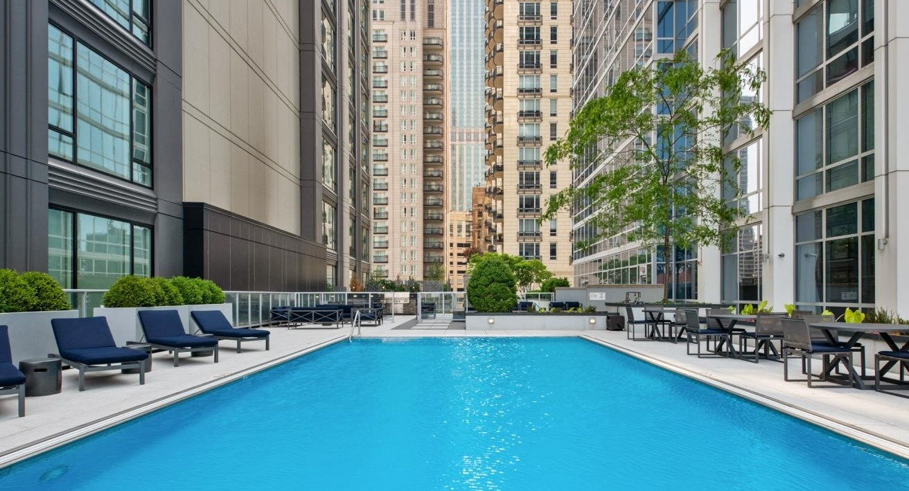 Refreshing outdoor swimming pool with lounge chairs, surrounded by modern high-rise buildings, offering a vibrant cityscape at Two West apartments in Chicago