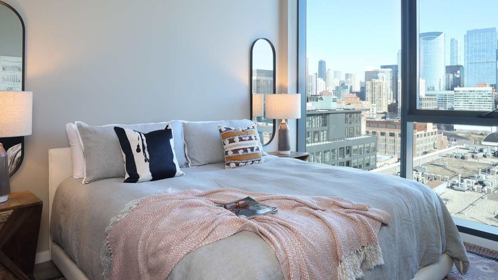 Cozy bedroom featuring a comfortable bed, stylish mirrors, and large windows offering impressive city views at Union West, Chicago
