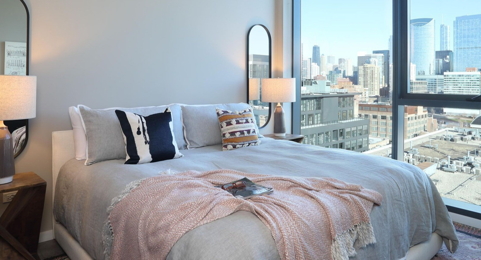 Cozy bedroom featuring a comfortable bed, stylish mirrors, and large windows offering impressive city views at Union West, Chicago