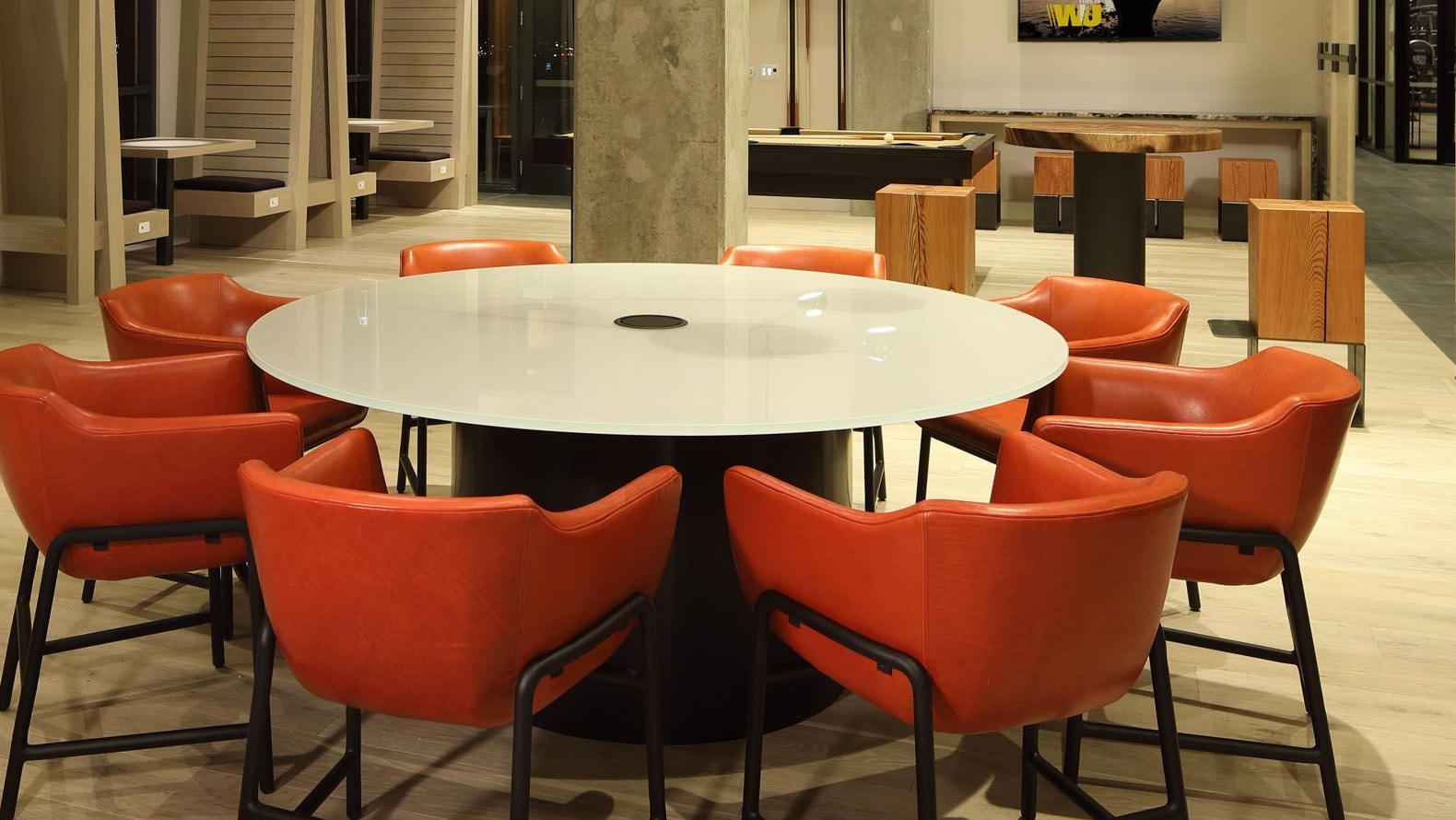 Vibrant community lounge with a large round table, striking orange chairs, and modern lighting at Union West, Chicago