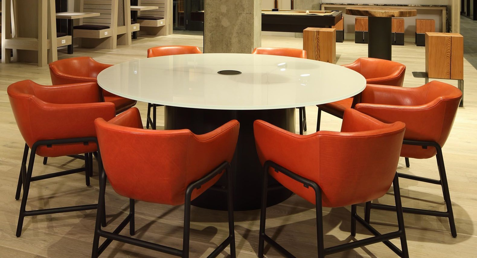 Vibrant community lounge with a large round table, striking orange chairs, and modern lighting at Union West, Chicago