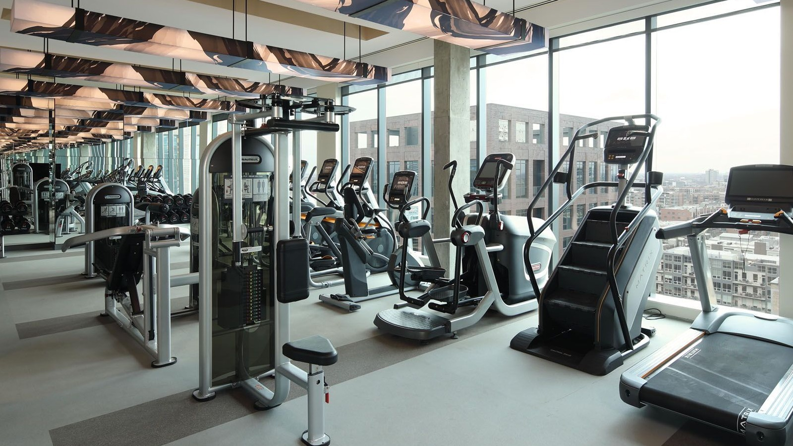 Expansive fitness center with various cardio machines and large windows offering city views at Union West apartments in Chicago