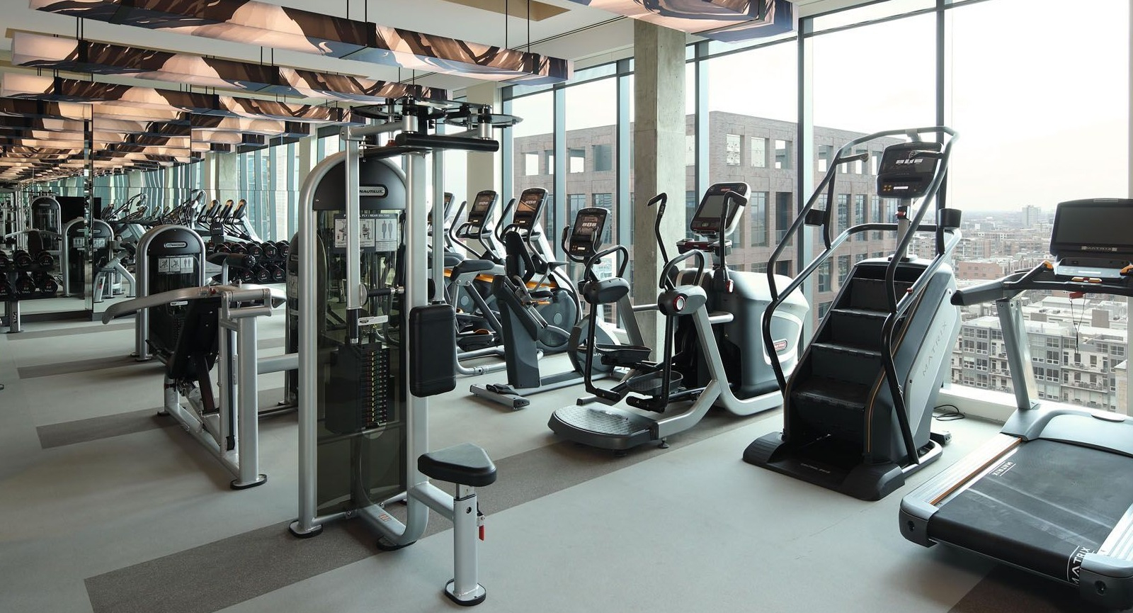 Expansive fitness center with various cardio machines and large windows offering city views at Union West apartments in Chicago