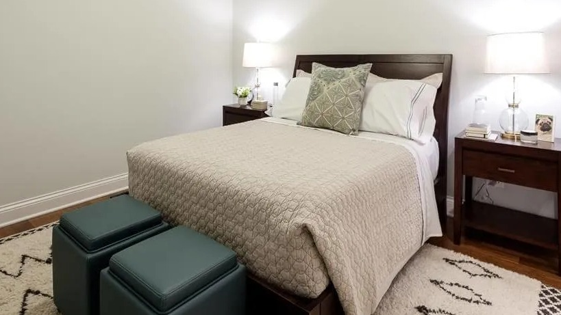 Cozy bedroom featuring a comfortable bed with neutral bedding, dark wood nightstands, and two teal ottomans at Wells Place, Chicago
