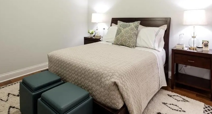 Cozy bedroom featuring a comfortable bed with neutral bedding, dark wood nightstands, and two teal ottomans at Wells Place, Chicago