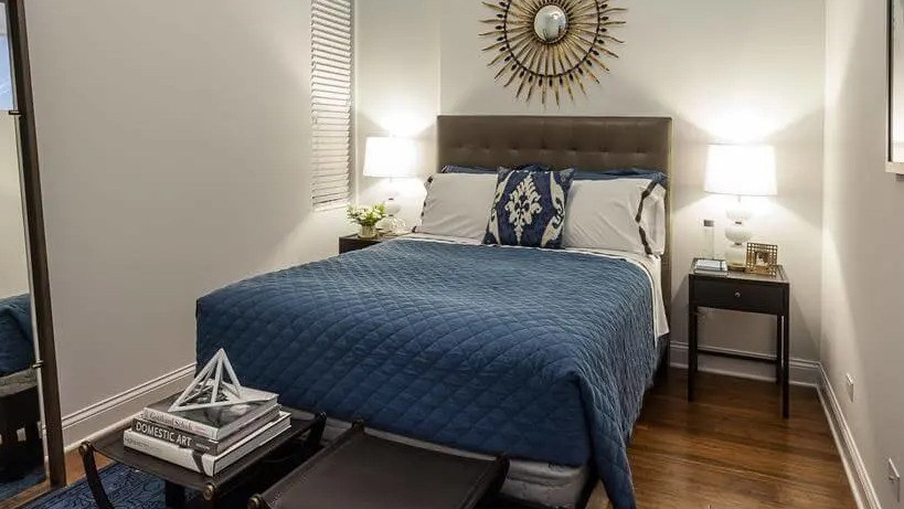 Stylish bedroom with a plush blue comforter, decorative mirror, and modern furnishings, offering a relaxing retreat at Wells Place, Chicago