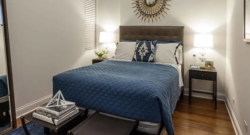 Stylish bedroom with a plush blue comforter, decorative mirror, and modern furnishings, offering a relaxing retreat at Wells Place, Chicago