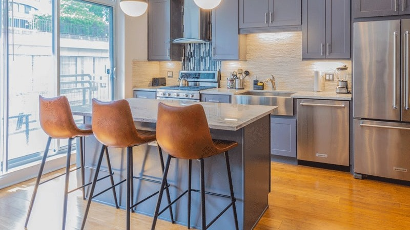 Bright apartment kitchen with grey cabinets, stainless steel appliances, and a large island with three bar stools at Wells Place, Chicago
