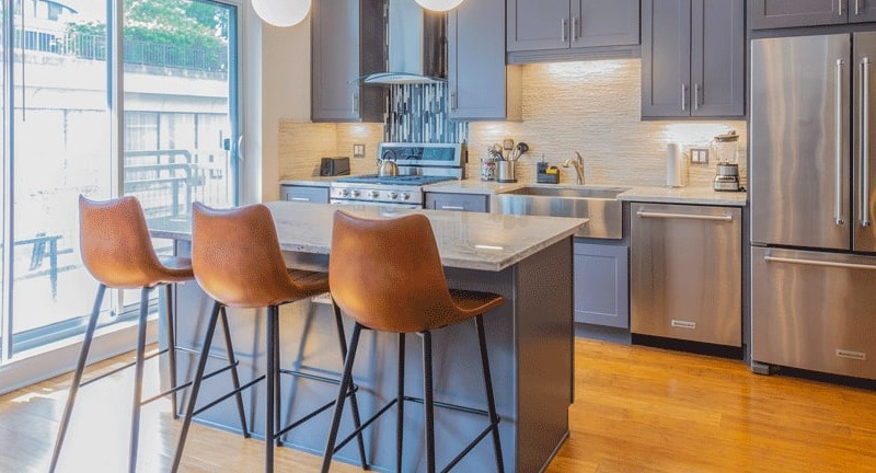 Bright apartment kitchen with grey cabinets, stainless steel appliances, and a large island with three bar stools at Wells Place, Chicago
