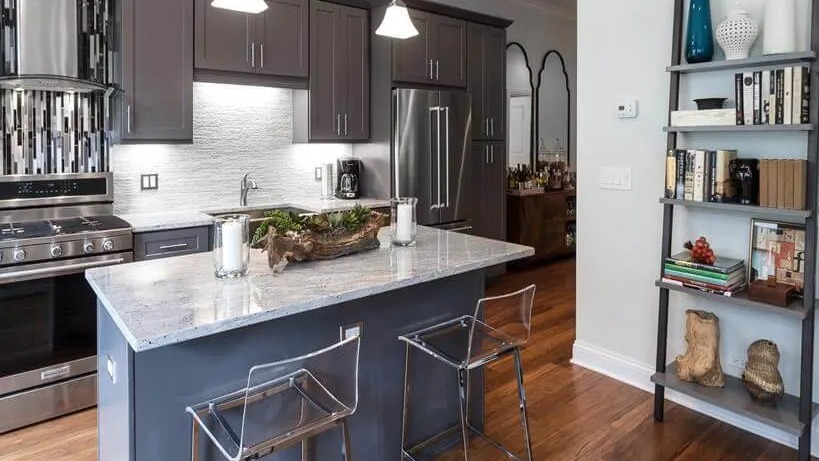 Modern kitchen with grey cabinetry, stainless steel appliances, and a central island with clear bar stools at Wells Place, Chicago