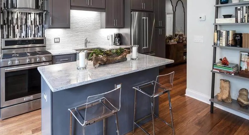 Modern kitchen with grey cabinetry, stainless steel appliances, and a central island with clear bar stools at Wells Place, Chicago