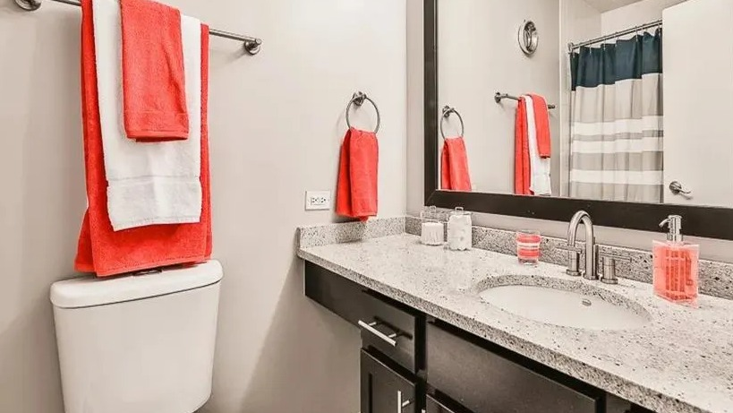 Modern bathroom with a spacious vanity, large mirror, and dark cabinets, accented with vibrant coral towels at West77, Chicago