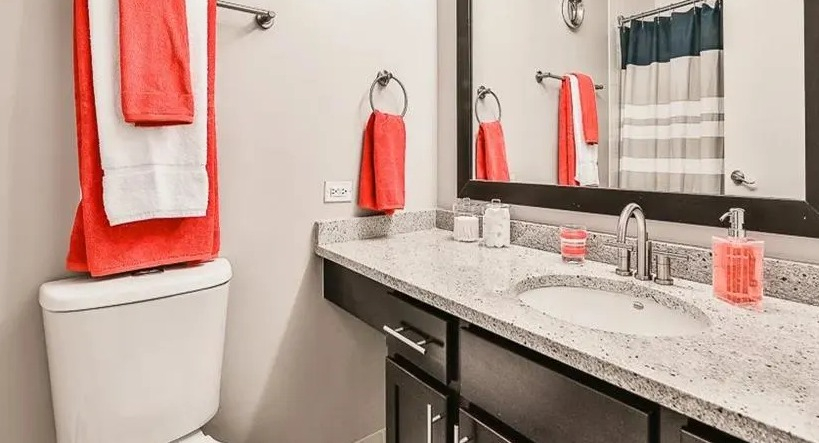 Modern bathroom with a spacious vanity, large mirror, and dark cabinets, accented with vibrant coral towels at West77, Chicago