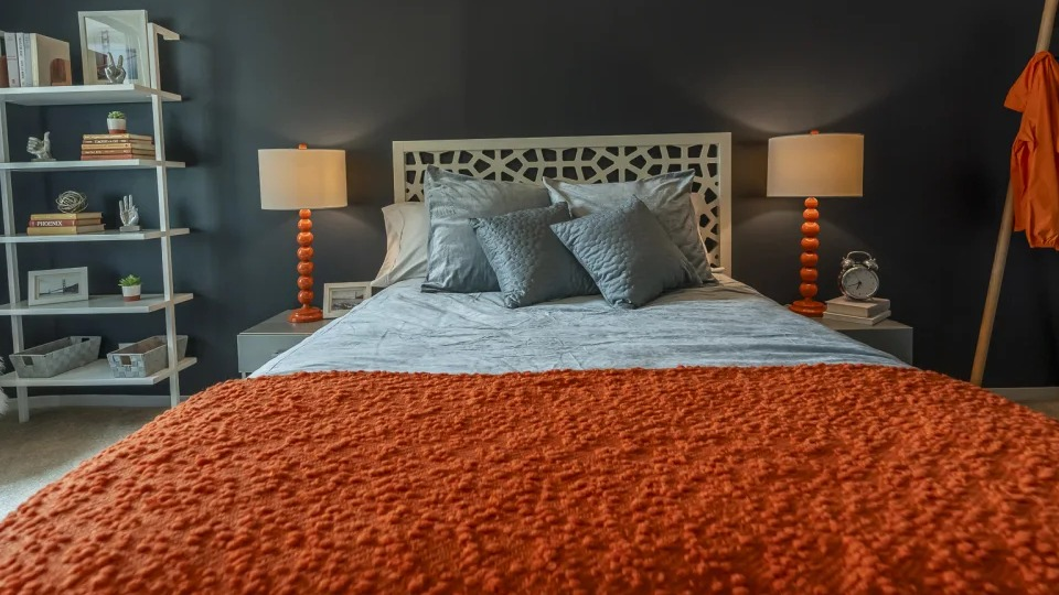 Vibrant bedroom with a dark accent wall, bright orange comforter, and a white decorative headboard at West77 Apartments in Chicago
