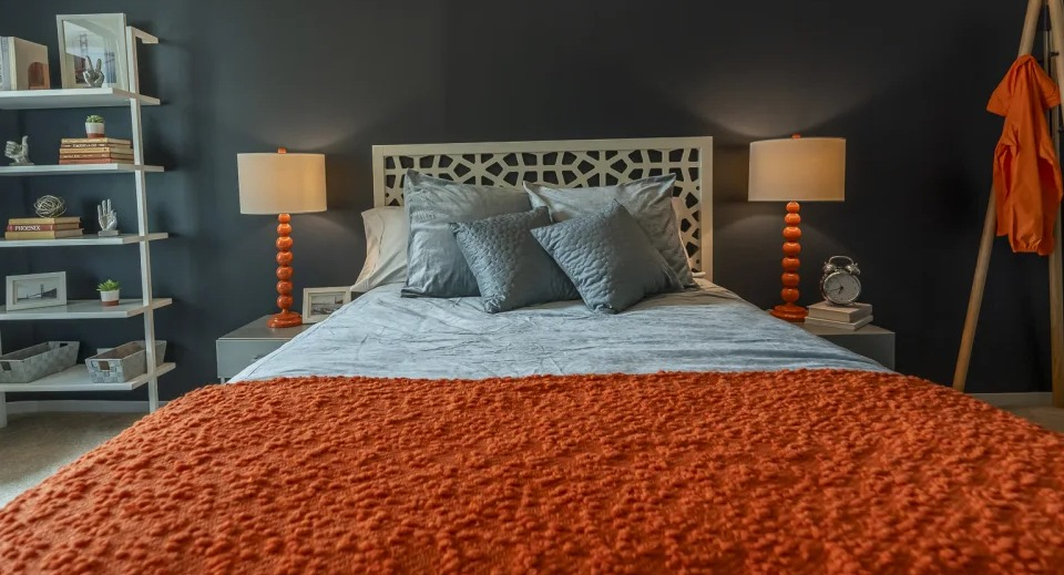Vibrant bedroom with a dark accent wall, bright orange comforter, and a white decorative headboard at West77 Apartments in Chicago