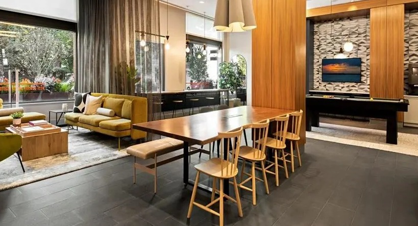 Expansive communal lounge area with a large dining table, comfortable seating, and a view of the game room at West77, Chicago