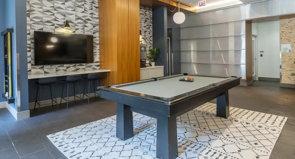 Modern game room with a billiards table, media wall, and stylish patterned accents at West77 Apartments in Chicago
