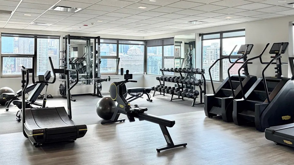 Comprehensive fitness center with a variety of cardio and strength training equipment, offering city views at West77 Apartments, Chicago