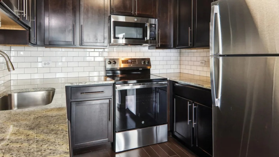 Apartment kitchen with dark wood cabinets, granite countertops, and stainless steel appliances at West77 Apartments in Chicago