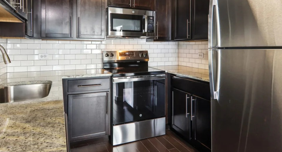 Apartment kitchen with dark wood cabinets, granite countertops, and stainless steel appliances at West77 Apartments in Chicago