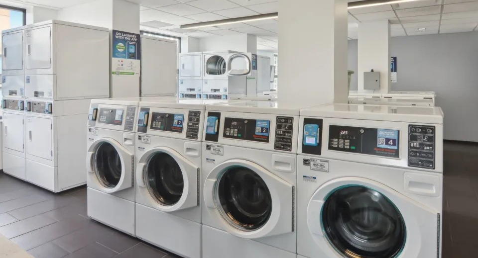 Modern and well-lit communal laundry room with multiple high-efficiency washers and dryers at West77 Apartments in Chicago