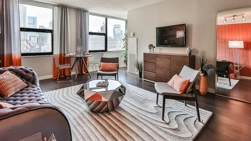 Stylish living room with unique furniture, a large mirror, and expansive city views from multiple windows at West77 Apartments, Chicago