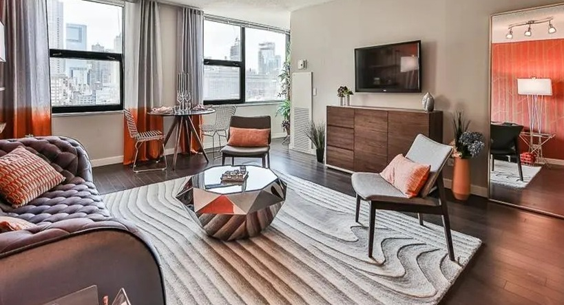 Stylish living room with unique furniture, a large mirror, and expansive city views from multiple windows at West77 Apartments, Chicago