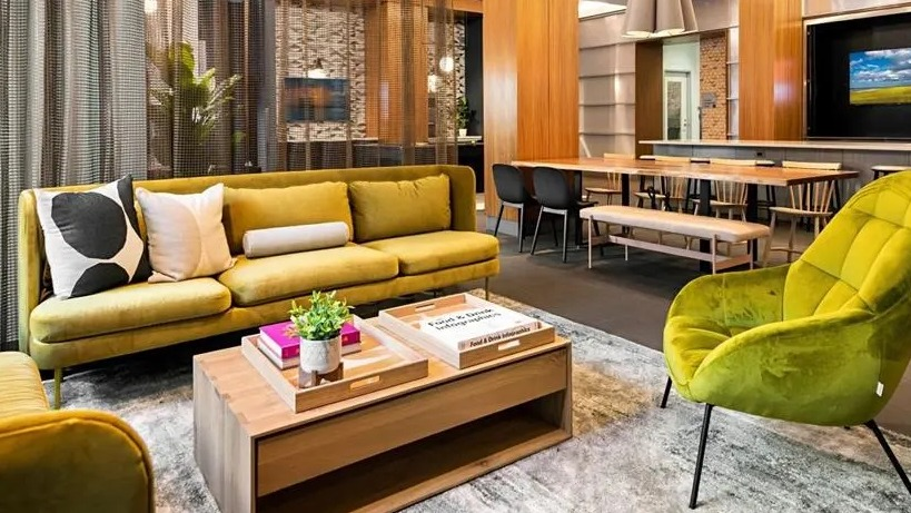 Vibrant resident lounge with comfortable yellow sofas, a large wooden table, and modern decor, perfect for socializing at West77, Chicago