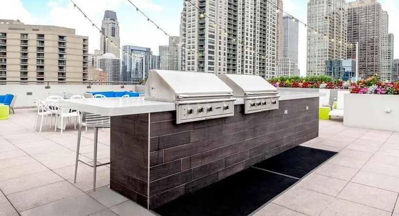 Expansive rooftop deck with grilling stations, outdoor seating, and panoramic Chicago skyline views at West77 Apartments