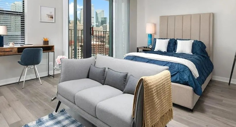Modern studio apartment with a comfortable bed, dedicated desk area, and a private balcony at West77 Apartments, Chicago