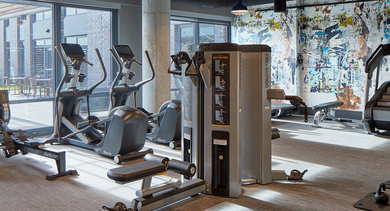 Dynamic fitness center with various cardio and weight machines, and a vibrant abstract mural wall at Westerly Apartments, Chicago