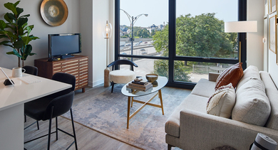 Modern living room with a compact kitchenette, comfortable seating, and large windows offering city views at Westerly, Chicago