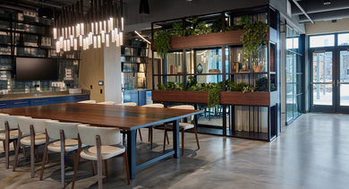 Expansive resident lounge with a long communal dining table, modern lighting, and an adjacent enclosed green space at Westerly, Chicago