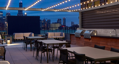 Enchanting rooftop deck at dusk with string lights, dining tables, grilling stations, and the Chicago skyline at Westerly apartments