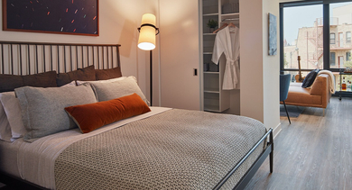 Functional studio apartment bedroom area with a comfortable bed, open closet storage, and adjacent living space at Westerly, Chicago