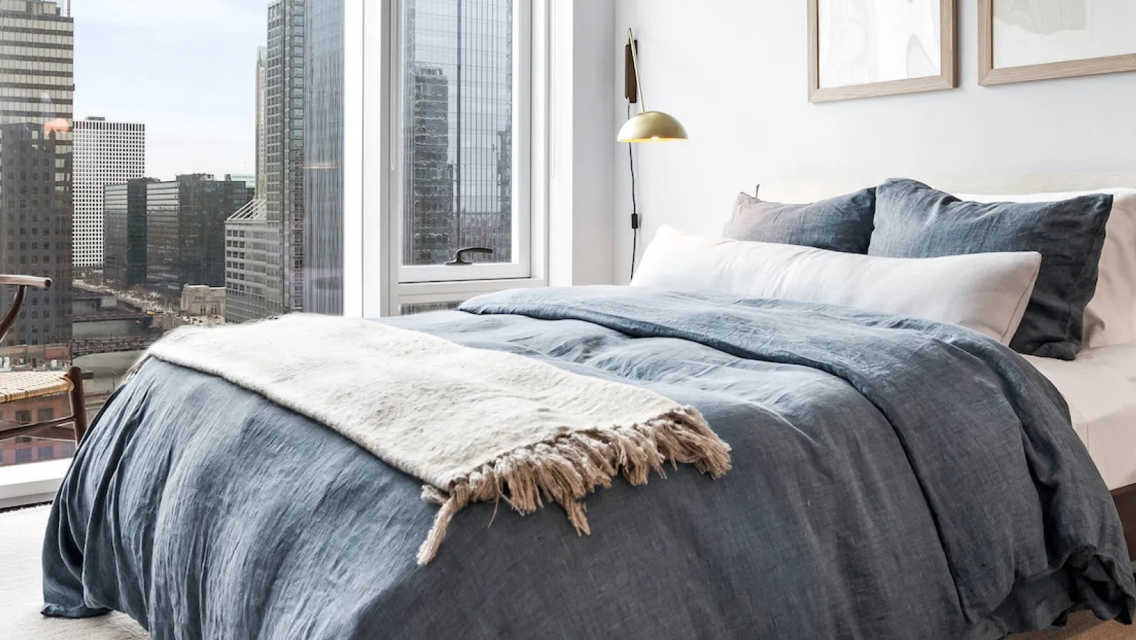 Cozy bedroom with a blue duvet, a wooden chair, and large windows offering stunning city views at Wolf Point East in Chicago