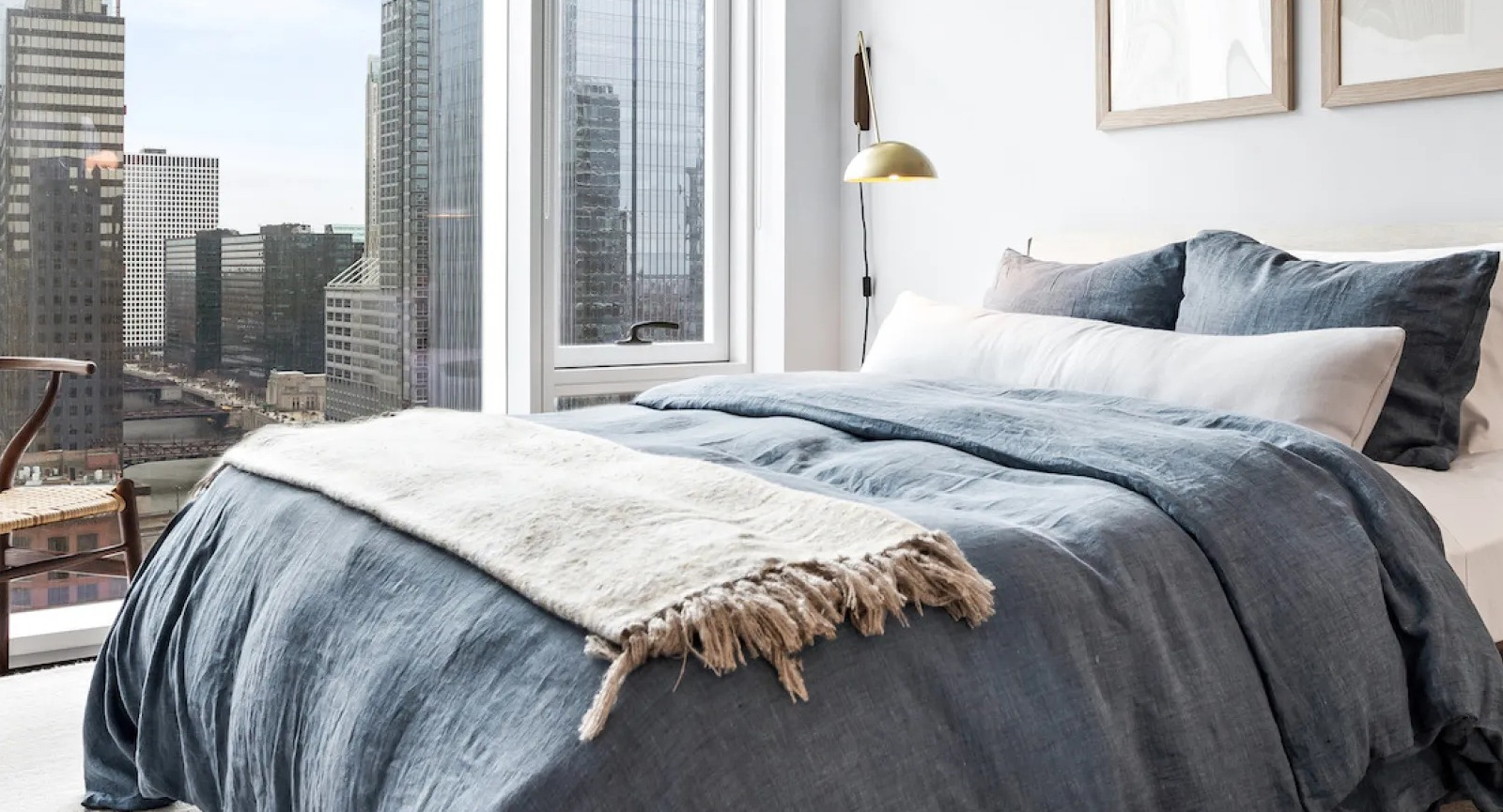 Cozy bedroom with a blue duvet, a wooden chair, and large windows offering stunning city views at Wolf Point East in Chicago